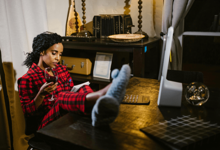 Black woman sits reading on chair with glass of wine and book